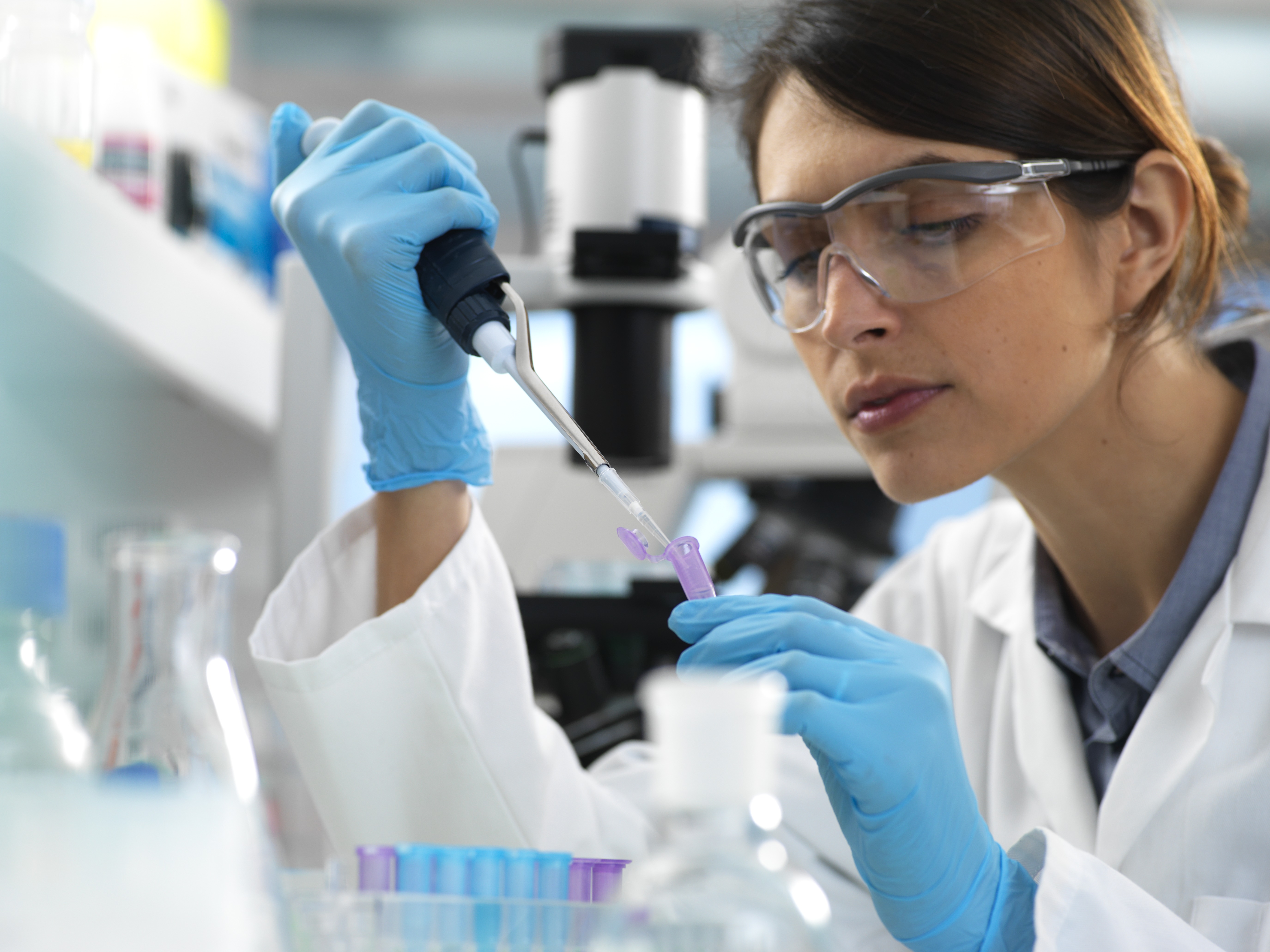 Scientist focusing in on a vail. She is using a pipette and is wearing ppe