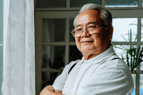 Older man standing next to a window with his arms crossed