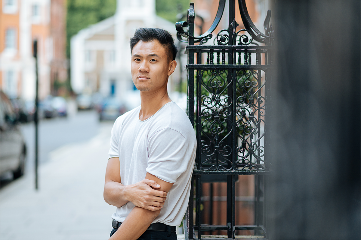 Young man holding his arm as he is leaning up against a fence