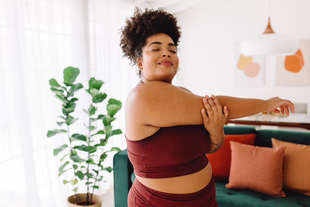 Plus size woman doing stretching workout at home. Beautiful healthy female in sports clothing working warm up workout indoors.