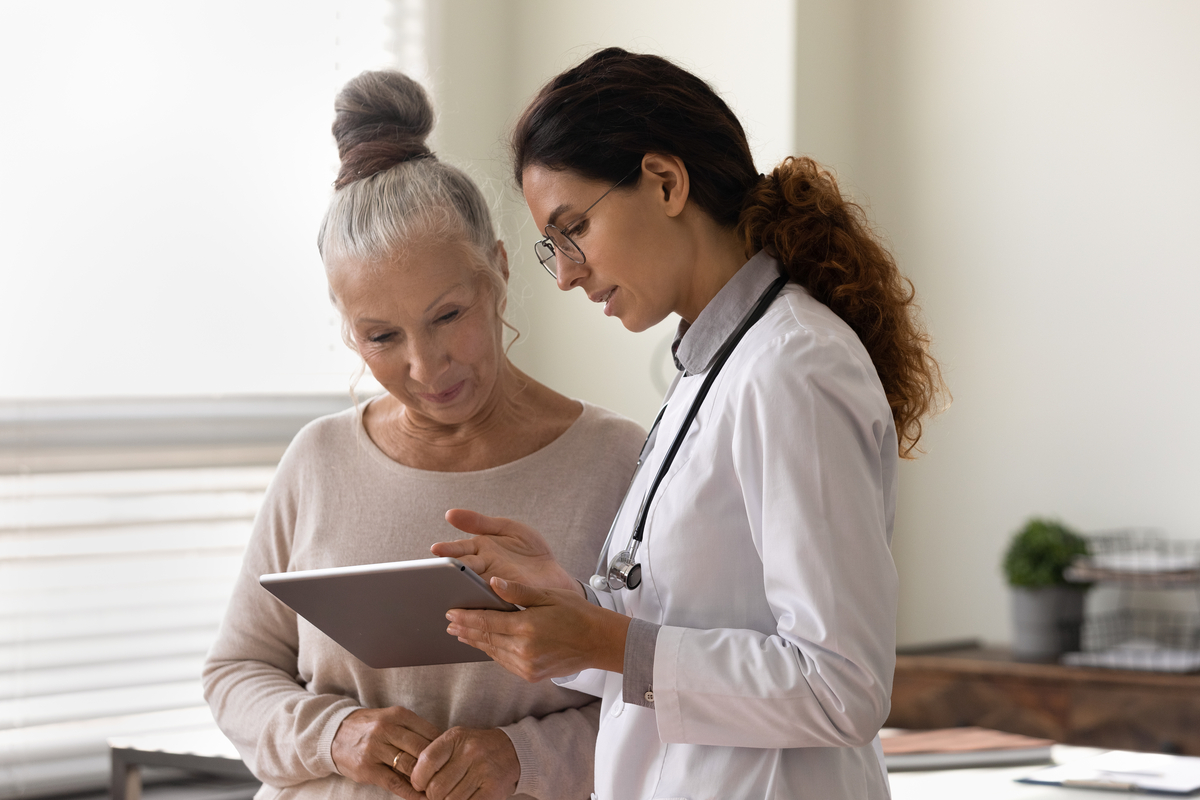 Young provider standing in an office with older patient. They are looking at a tablet